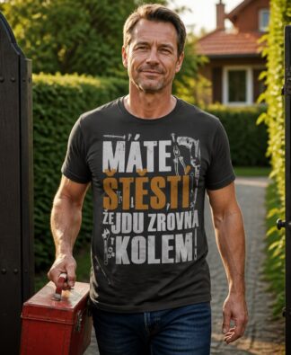 Muž s kufříkem nářadí prochází brankou v tmavě šedém tričku s nápisem Máte štěstí, že jdu zrovna kolem